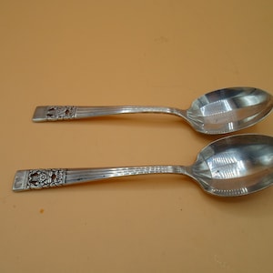 May include: Two silver spoons with ornate handles. The spoons have a slightly rounded shape and a smooth, polished finish.