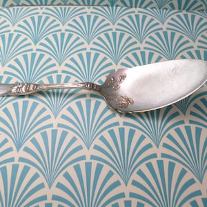 May include: A silver cake server with an ornate handle and a slightly curved blade. The server is on a white and blue patterned surface.