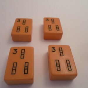 May include: Four orange dominoes with black dots. Each domino has three dots, arranged in a vertical line with the number "3" at the top.