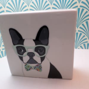 May include: White ceramic square box with a black and white image of a French bulldog wearing green glasses and a colorful bow tie.