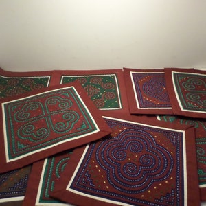 May include: A set of eight embroidered fabric squares with intricate geometric patterns in shades of red, green, blue, and white. The squares are arranged in a staggered pattern.