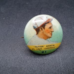 Może przedstawiać: Vintage przypinka baseballowa z portretem "Pepper" Martin z St. Louis Cardinals. Przypinka ma zielono-ż&oacute;łtą obw&oacute;dkę z numerem 21. Obraz przedstawia profil baseballisty.