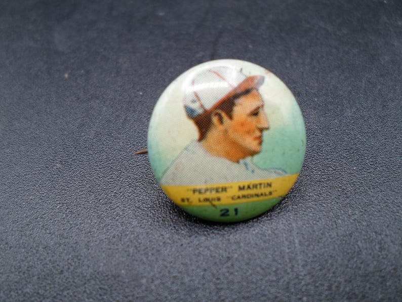 Może przedstawiać: Vintage przypinka baseballowa z portretem "Pepper" Martin z St. Louis Cardinals. Przypinka ma zielono-ż&oacute;łtą obw&oacute;dkę z numerem 21. Obraz przedstawia profil baseballisty.