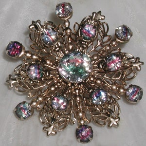 May include: A gold-toned snowflake brooch with iridescent glass stones. The stones are a mix of pink, purple, and green.