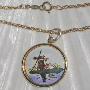 May include: A gold chain necklace with a round pendant featuring a painted image of a windmill on a canal. The pendant has a gold rim.