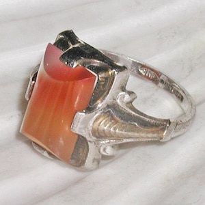 Puede incluir: Un anillo de plata con una piedra preciosa naranja y blanca engastada en un diseño filigranado detallado.