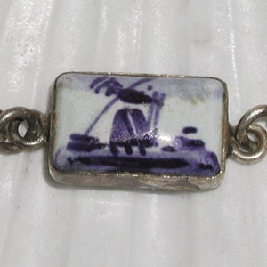 May include: A silver chain bracelet with a rectangular blue and white enamel charm featuring a windmill design.