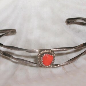 May include: A silver twisted wire bracelet with a red coral stone in the center.