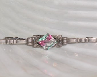 May include: A silver brooch with a square-shaped, multi-colored glass stone in the center.