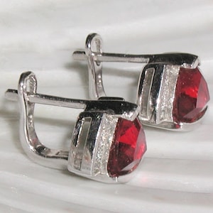 May include: A pair of silver earrings with red gemstone accents. The earrings have a simple hoop design with a small, faceted red stone set in the center of each hoop.