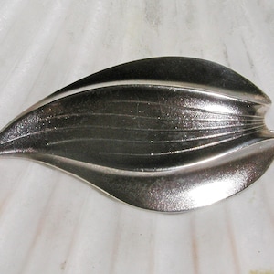 Puede incluir: Un broche de plata en forma de hoja con una superficie texturizada.