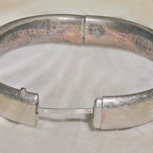 May include: A silver hinged bangle bracelet with a simple design. The bracelet has a clasp with the inscription "925" on it.