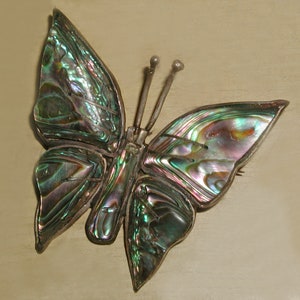 Puede incluir: Un broche de mariposa de plata con alas de nácar de abulón verde y azul iridiscente.