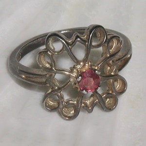 May include: A silver ring with a delicate floral design and a pink gemstone in the center.