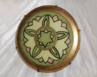 May include: A round, gold-rimmed brooch with a green and white floral design. The center of the brooch features a green star.