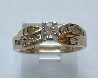 May include: A gold ring with a single round diamond in the center and smaller diamonds set in the band.