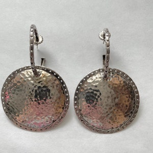 Pode incluir: Um par de brincos de argola de prata com um pingente redondo martelado. Os brincos têm um design de corrente.