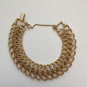 Puede incluir: Un brazalete de cadena dorado con un diseño delicado e intrincado. El brazalete está hecho de múltiples bucles enlazados, creando un efecto de capas.