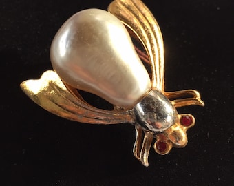 May include: A gold-tone brooch in the shape of a fly with a large, pearlescent white body and red rhinestone eyes.