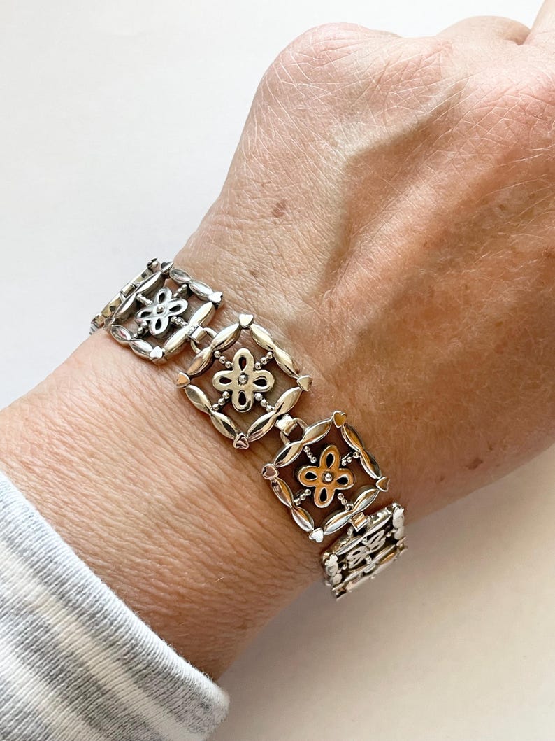 以下が含まれることがあります： 花柄のスクエアリンクが繰り返されるシルバーブレスレット。ブレスレットはシルバーとゴールドの2種類の金属で作られています。