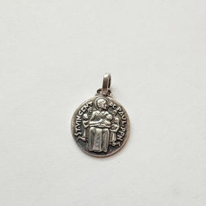May include: A silver-toned pendant with a detailed image of a religious figure, inscribed with the text "ST. VINCENT DE PAUL PPN." The pendant has a loop at the top for a chain and is likely made of metal.