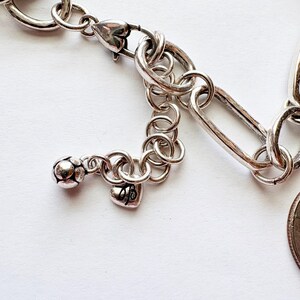 Puede incluir: Primer plano de una pulsera plateada con un dije en forma de coraz&oacute;n y un cierre de mosquet&oacute;n. La pulsera presenta una mezcla de dise&ntilde;os de eslabones ovalados y alargados, con un peque&ntilde;o dije de coraz&oacute;n y una bola decorativa.