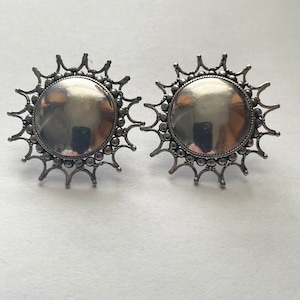 May include: A pair of silver earrings with a sunburst design. The earrings are round and have a smooth, polished finish.