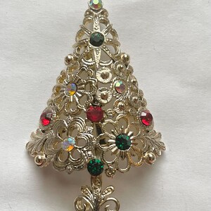 May include: A gold-tone Christmas tree brooch with red, green, and iridescent rhinestones.