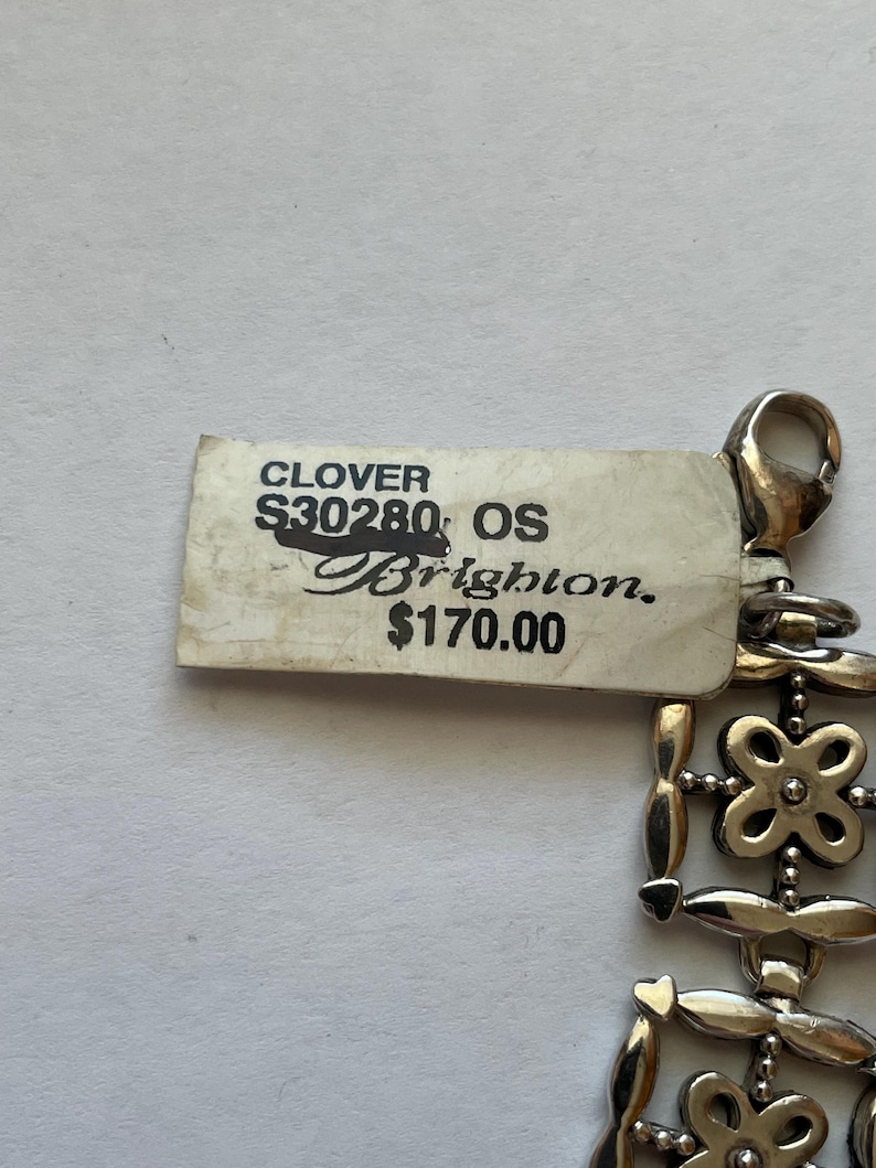 以下が含まれることがあります： クローバーのデザインのシルバーブレスレット。ブレスレットに付けられたタグには、「CLOVER S30280 OS Brighton 170.00ユーロ」と記載されています。
