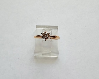 May include: A gold band ring with a single, round, clear diamond in the centre.
