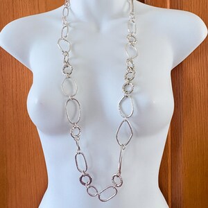 Puede incluir: Collar plateado con una variedad de formas geom&eacute;tricas, incluyendo &oacute;valos, c&iacute;rculos y rect&aacute;ngulos. El collar se exhibe en un maniqu&iacute; blanco, mostrando su longitud y dise&ntilde;o. Una pieza de joyer&iacute;a llamativa.