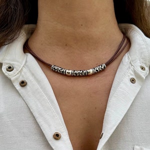 May include: A brown leather necklace with silver beads featuring a floral design. The necklace is layered with two strands of leather.