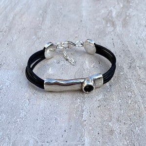 May include: A black leather bracelet with a silver bar and a black gemstone. The bracelet has a silver clasp.