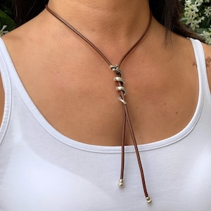 May include: A brown leather choker necklace with a silver twisted metal accent. The necklace has two silver beads at the ends.