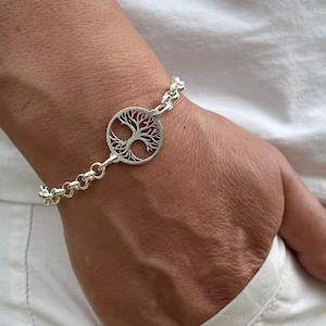 May include: A silver bracelet featuring a tree of life charm. The chain is a curb link style.