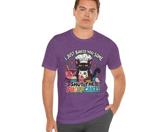 Puede incluir: Una camiseta de manga corta en color morado jaspeado con un gráfico de un gato negro con gorro y delantal de chef. El gato está rodeado de cupcakes y un bol. El texto dice: I JUST BAKED YOU SOME SHUT THE FUCUPCAKES.