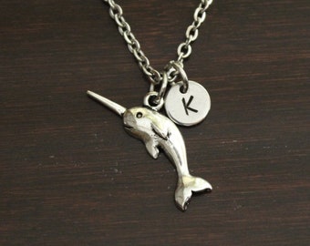May include: Silver narwhal necklace with a silver initial charm. The initial charm is a letter K.