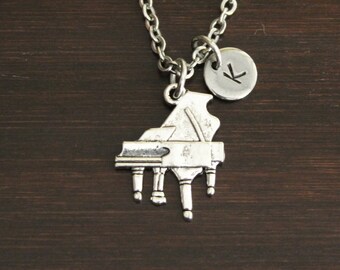 May include: A silver necklace with a piano charm and a silver disc charm with the letter "K" engraved on it.