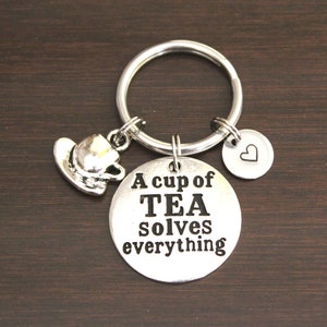 May include: Silver keychain with a charm that says "A cup of TEA solves everything" and a small teacup charm. There is also a small heart charm on the keychain.