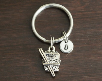 May include: Silver keychain with a charm of a takeout container with chopsticks and the words "Food to Go". A silver charm with the letter "O" is also attached to the keychain.