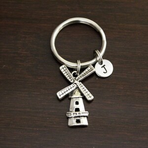 May include: Silver keychain with a windmill charm and a letter 'J' charm. The keychain is on a dark brown wooden surface.