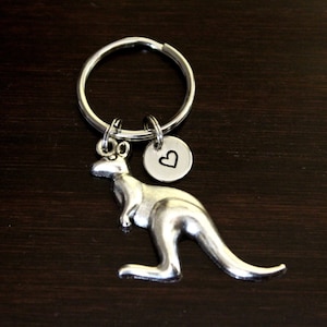 May include: Silver kangaroo keychain with a heart charm. The keychain is on a dark brown wooden surface.