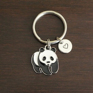 May include: A silver key chain with a black and white panda charm and a small silver charm with a heart engraved on it.