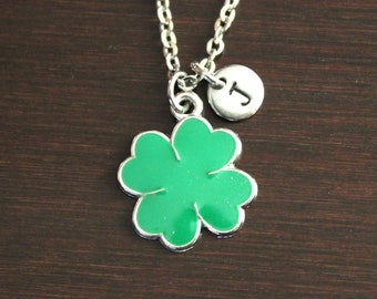 May include: A silver chain necklace with a green four-leaf clover charm and a silver charm with the letter "J" on it.