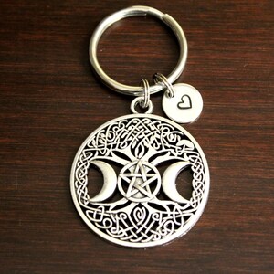 May include: Silver-toned keychain featuring a triple moon and pentacle design with a Celtic knot border. A small heart charm is attached to the keychain ring.
