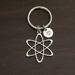 Puede incluir: Llavero de plata en forma de &aacute;tomo con un peque&ntilde;o dije en forma de coraz&oacute;n. El &aacute;tomo es una representaci&oacute;n estilizada de un &aacute;tomo con un n&uacute;cleo y electrones en &oacute;rbita.