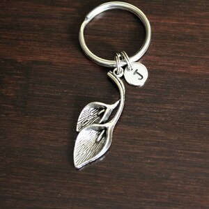 May include: Silver key chain with a charm of two stylized calla lilies and a small round charm with the letter J.
