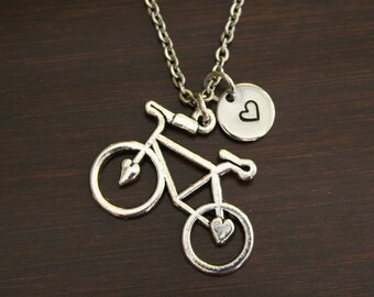 May include: A silver necklace with a bicycle charm and a small heart charm. The bicycle charm is detailed with a heart on each wheel.