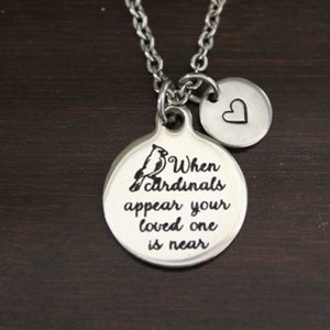 May include: Silver necklace with two charms. The larger charm is round and features a cardinal bird and the text "When cardinals appear your loved one is near". The smaller charm is a heart.