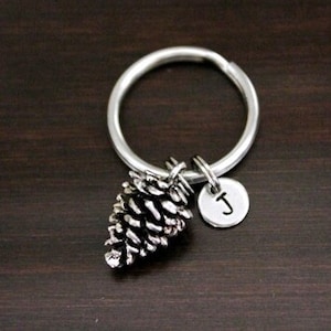 May include: Silver keychain with a pine cone charm and a silver disc charm with the letter J.